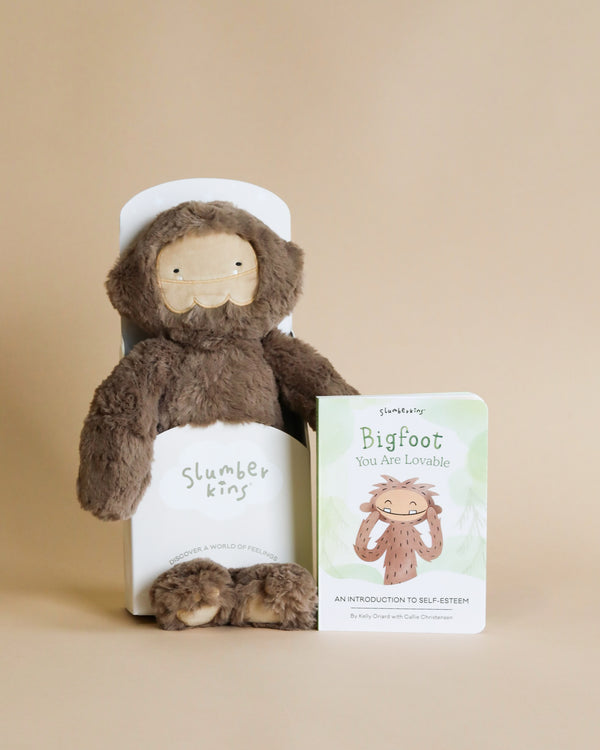 A Slumberkins Bigfoot Kin + Lesson Book On Self Esteem, filled with hypoallergenic fiberfill, alongside a book titled "Bigfoot You Are Lovable: An Introduction to Self-Esteem" against a