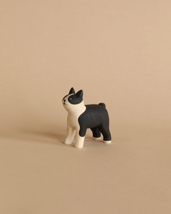 A hand-painted wooden figurine of a Boston Terrier with a playful stance, set against a plain beige background.