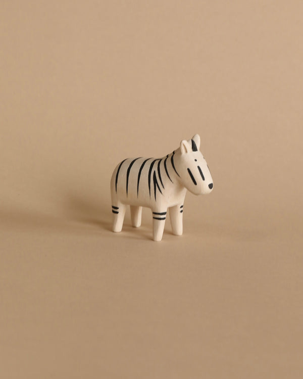 A small Tiny Wooden Zebra figurine with distinct black stripes on a beige background. The zebra is facing left and stands in a neutral posture.