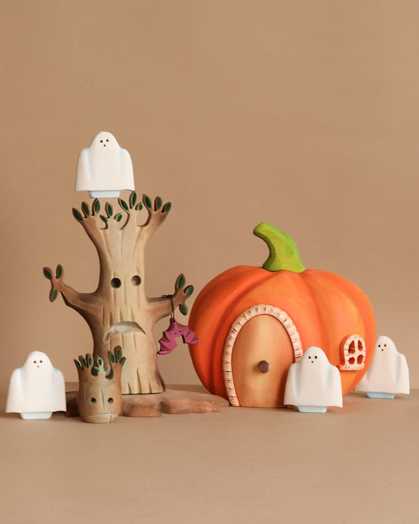 The Bumbu Handmade Wooden Haunted Pumpkin Cottage Set features a wooden tree, a handmade pumpkin house, and five white ghost figurines, all arranged for whimsical Halloween fun and perfect for Montessori imaginative play.