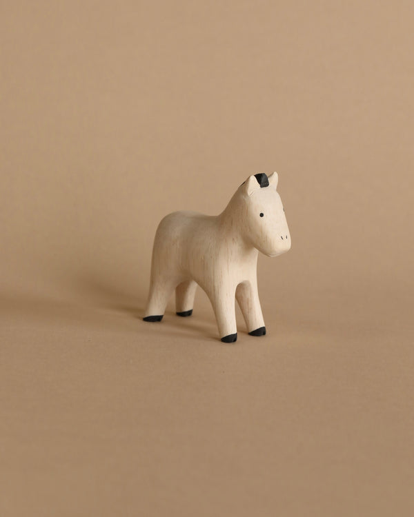 A handmade tiny wooden farm animal horse with a simplistic design and natural wood finish, standing on a beige background. The horse features painted black details on the hooves and ears.