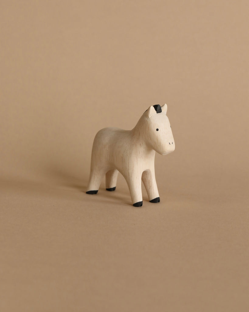 A handmade tiny wooden farm animal horse with a simplistic design and natural wood finish, standing on a beige background. The horse features painted black details on the hooves and ears.