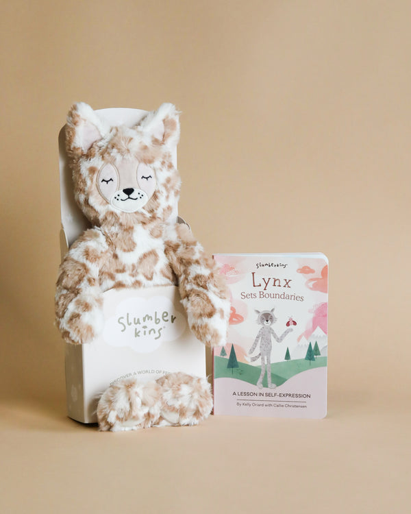 Plush lynx toy seated next to its illustrated storybook, "Lynx Sets Boundaries", against a beige background. The book and hypoallergenic stuffed animal are part of the Slumberkins Lynx Kin + Lesson Book On Self Expression.