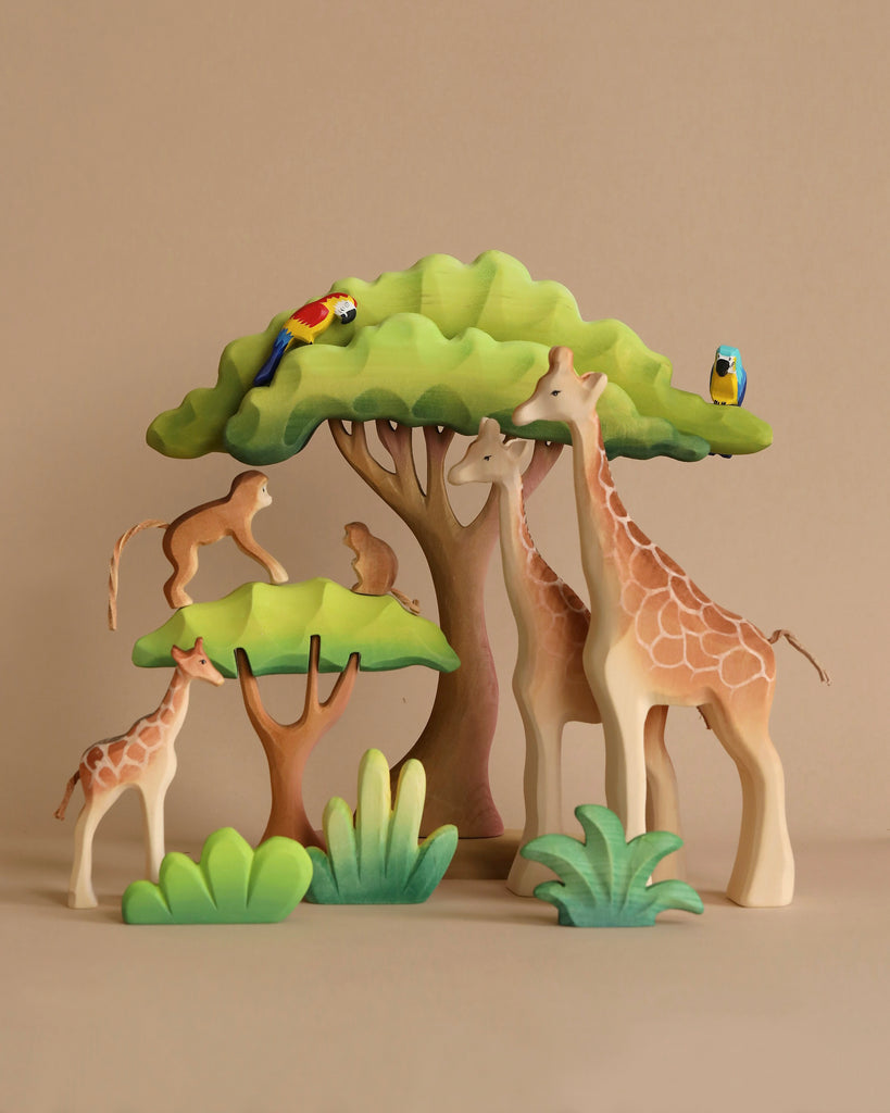 Wooden animal toys, including the Bumbu Wooden Giraffe Family Set, monkeys, and birds, are set against a backdrop of stylized trees and greenery on a plain background. The figures are artistically crafted from organic wood and arranged to create a playful jungle scene that promotes Montessori play.