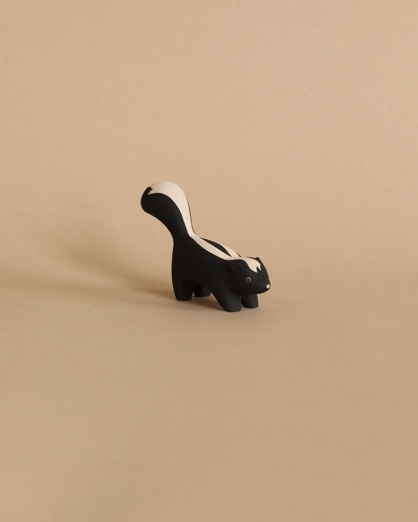 A small, Handmade Tiny Wooden Forest Animals - Skunk figurine positioned on a plain beige background, casting a soft shadow.