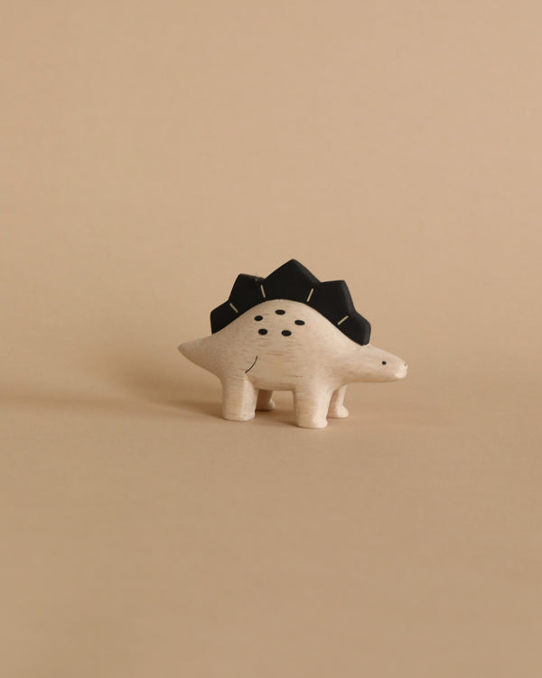 A Handmade Tiny Wooden Dinosaurs - Stegosaurus toy, resembling a stegosaurus with black spikes, stands against a plain beige background. It features dot eyes and a small, drawn smile.