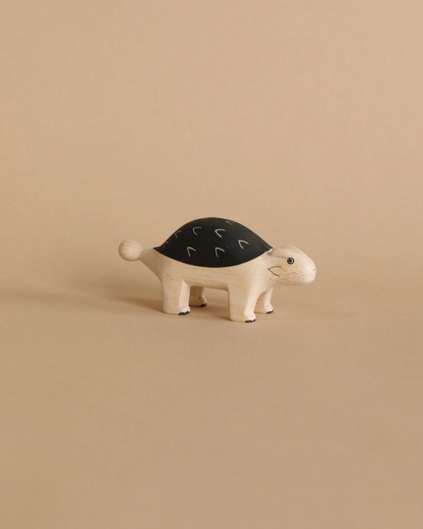 A handcrafted wooden Ankylosaurus, made by Bali artisans from Albizia wood, with a black shell featuring white squiggle patterns stands against a plain beige background. The Ankylosaurus has a friendly expression.
