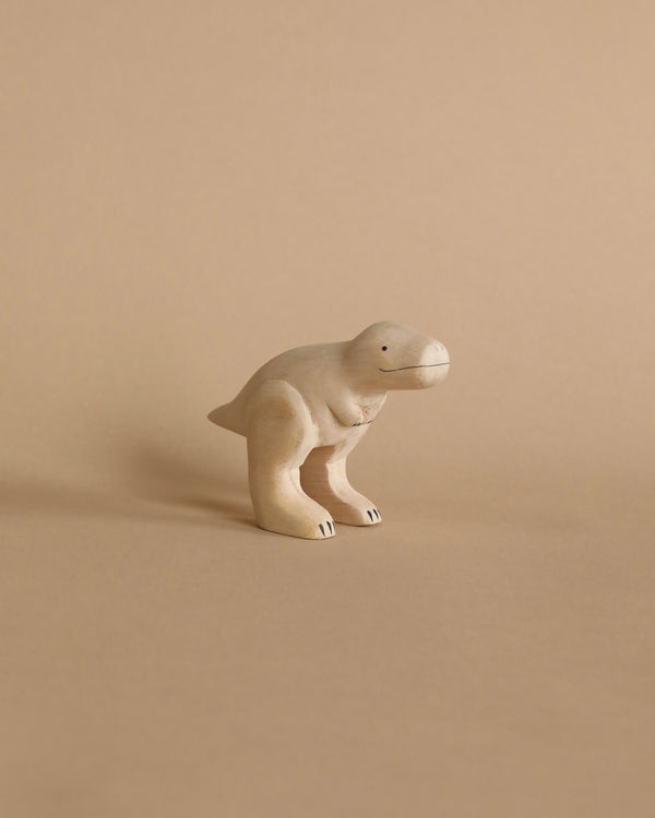 A Handmade Tiny Wooden Dinosaurs - T-Rex toy, shaped like a tyrannosaurus rex, stands on a plain beige background. The toy is handcrafted from Albizia wood with smooth curves and subtle painted details.