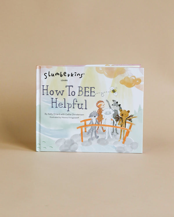 A children's book titled "Slumberkins How To Bee Helpful Book" displayed upright against a beige backdrop, featuring colorful illustrations of cartoon animals and bees on the cover, teaching lessons of teamwork.