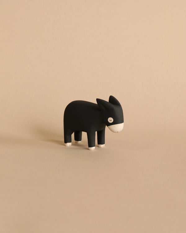 A minimalist, handcrafted black wooden figurine of a Donkey, set against a plain beige background, displaying simplistic design with visible wood grain on its face.