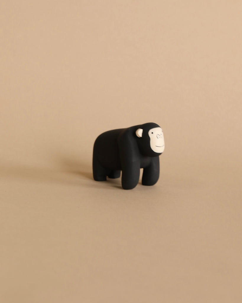 A tiny gorilla from the Handmade Tiny Wooden Safari Animals collection stands on a neutral beige background. The small, black figurine features a simple design with a white face and white ear details, exuding a minimalistic and cute charm reminiscent of hand-painted animal figurines.