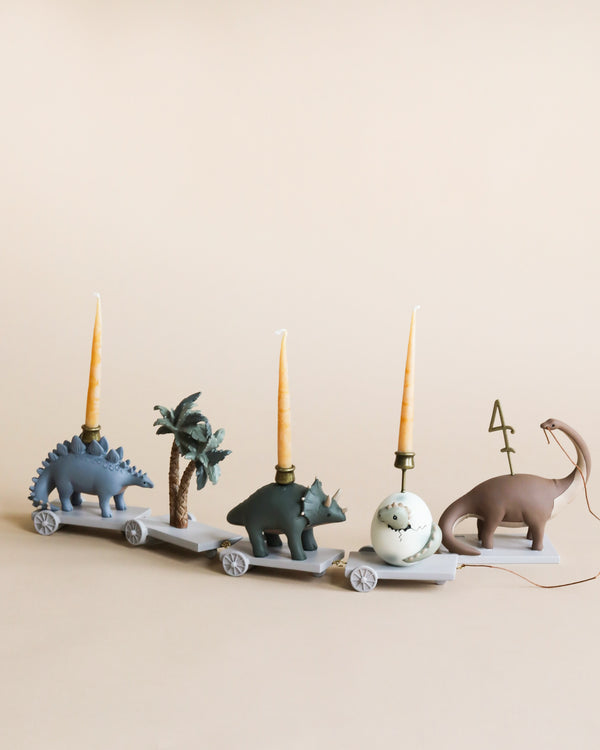 Four whimsical candle holders shaped like animals—a Dinosaur Birthday Train With Beeswax Candles, a rhinoceros, an elephant, and a camel—aligned on a light background, each with a tall beige candle in a dinosaur theme