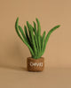 A Handmade Felt Herb Pot, featuring a small tan container labeled "CHIVES" with green felt leaves sprouting out, crafted from sustainable materials, sits against a plain beige background. Perfect for a pretend kitchen setup.