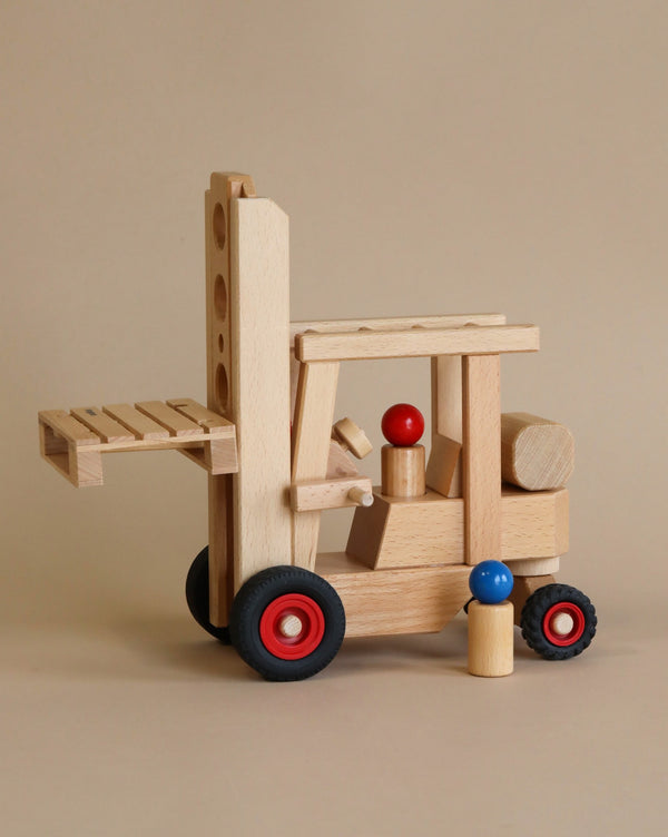A Fagus Wooden Forklift toy with red and blue details against a beige background. The forklift features moving parts, including a lifting mechanism and wheels.