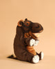 The Hippo Puppet, part of the HANSA animals collection, features brown and tan fur, white feet, and an open mouth with white teeth. It sits upright on a beige surface against a matching background for a lifelike display.