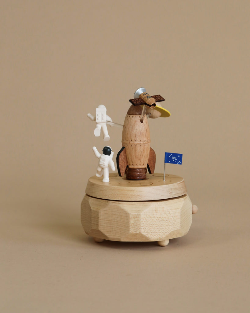 Space themed wooden music box with a rocket in the middle and astronauts and spaceships going around it. 