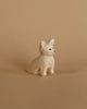 A small, handcrafted figurine of a Handmade Tiny Wooden Chihuahua with delicate facial features sitting against a plain beige background. The Chihuahua, carved from Albizia wood, has subtle black detailing for its eyes, whisk.