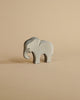 A Ostheimer Small Elephant - Eating figurine stands against a plain beige background, showcasing its stylized shape and subtle wood grain texture.