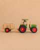 A Maileg x Fagus Limited Edition Tractor Set, featuring a green-cab wooden tractor with red wheels and a detachable trailer, is driven by a Maileg Hiker Mouse on a beige background.