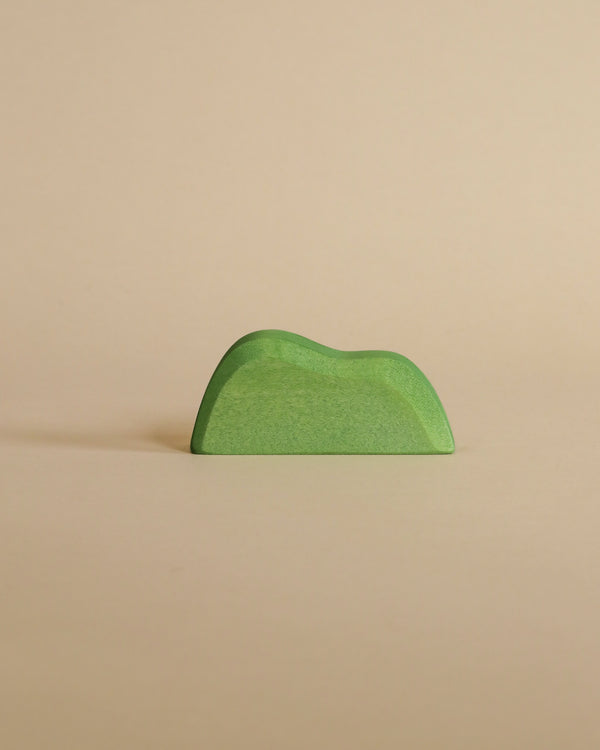A small, green, minimalist handcrafted Ostheimer Bush shaped like a hill, placed against a plain beige background.