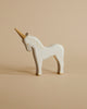A handcrafted Ostheimer Unicorn with a natural finish stands on a beige background. The unicorn features painted eyes and a simple, stylized horn.