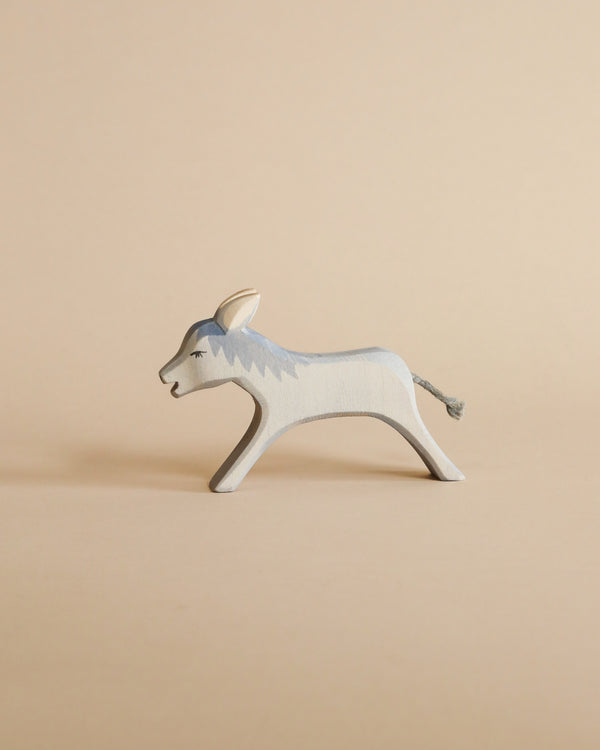A handcrafted Ostheimer Donkey Running painted in shades of gray and white, placed against a plain beige background. The donkey is in a walking pose with detailed facial features.