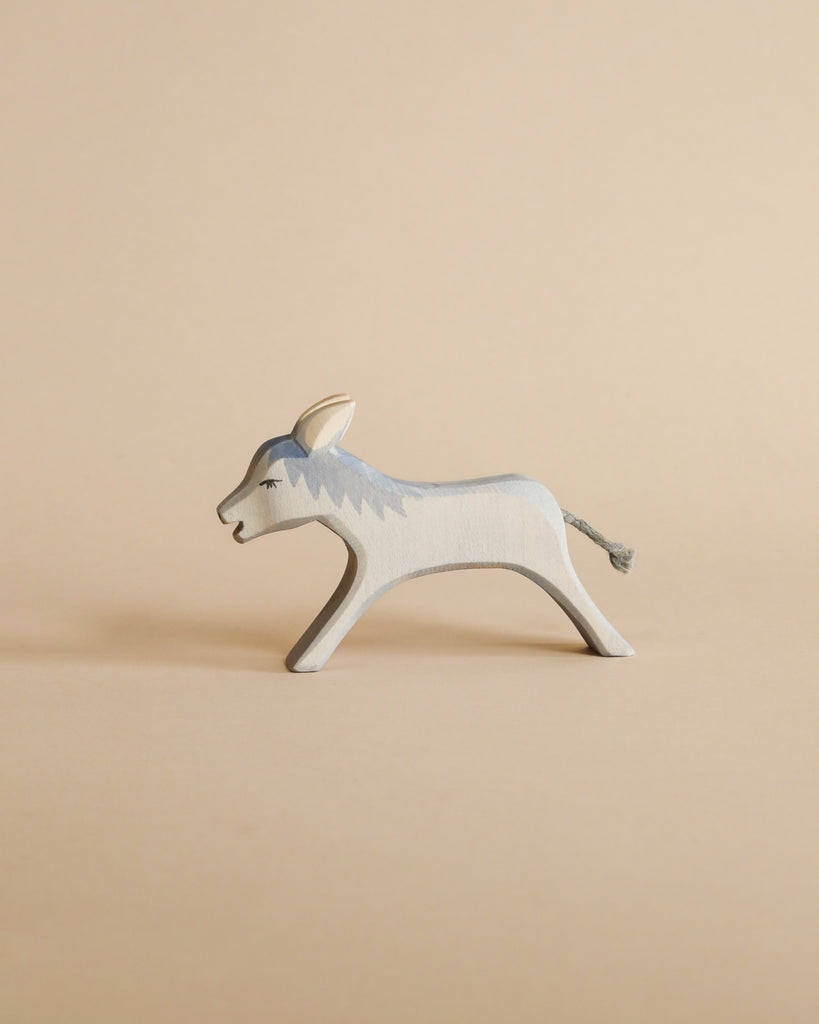 A handcrafted Ostheimer Donkey Running painted in shades of gray and white, placed against a plain beige background. The donkey is in a walking pose with detailed facial features.