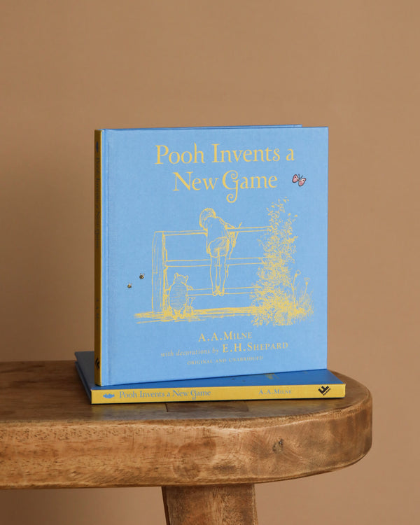 A blue hardcover book, "Winnie-the-Pooh: Pooh Invents a New Game," rests on a wooden surface with gold illustrations—a delightful addition to any collection of classic children's stories or bedtime favorites.