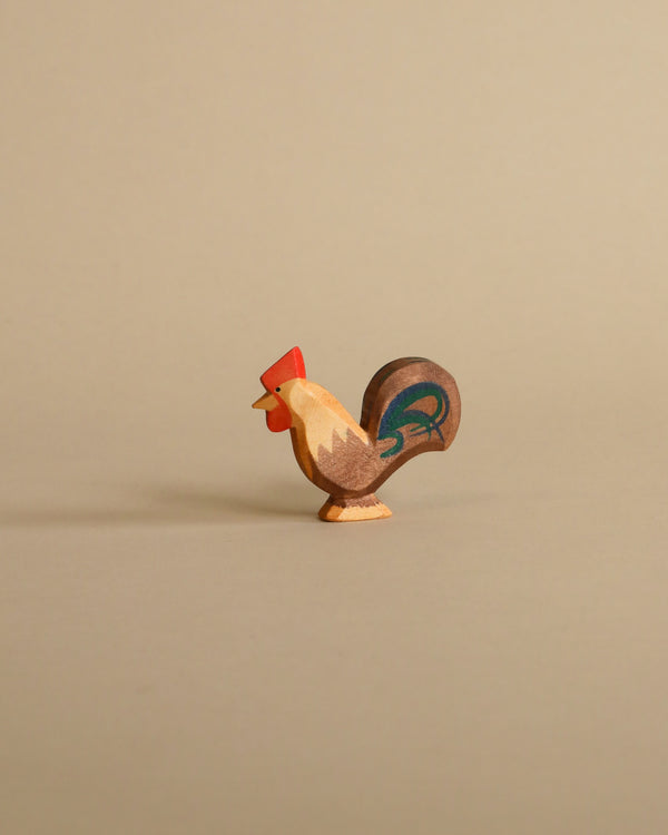 A handcrafted Ostheimer Rooster - Brown figurine stands on a plain beige background, featuring a red head, beige body, and a tail with blue and green accents.