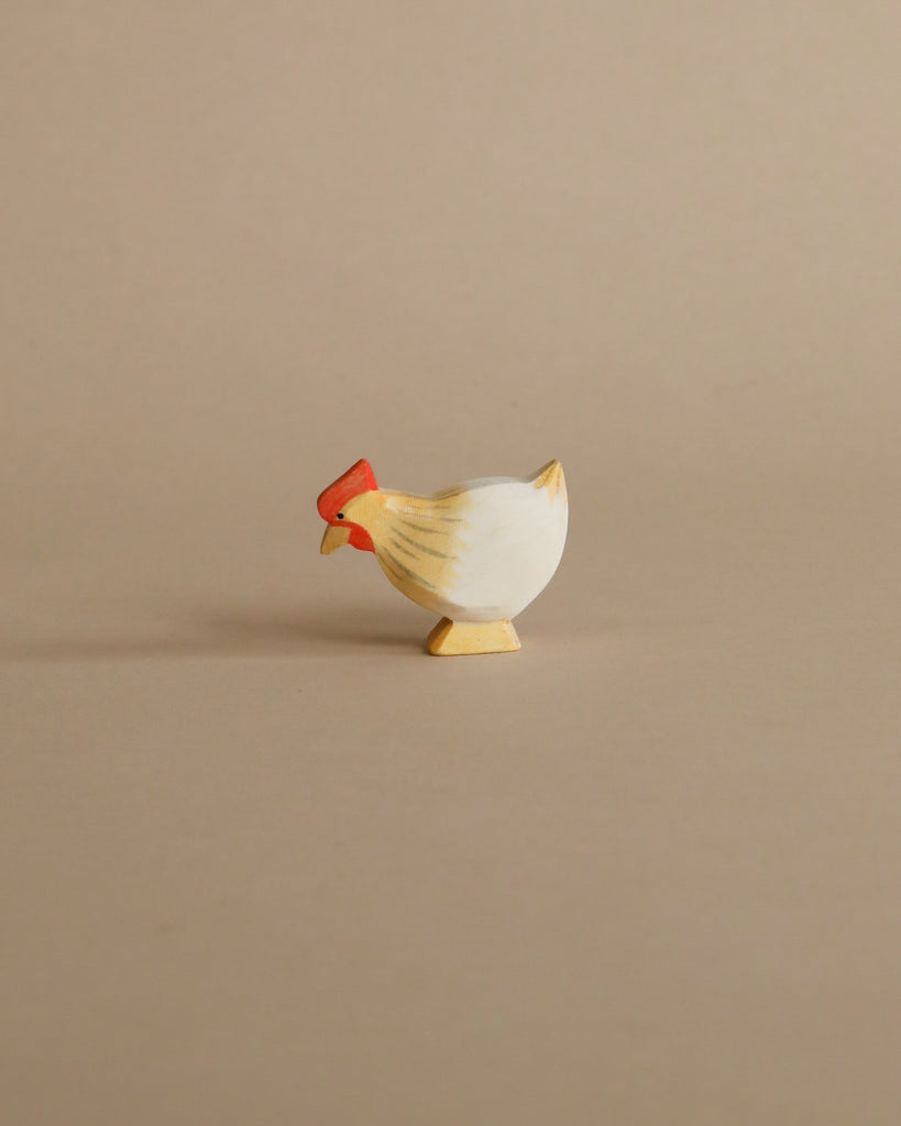 From the Enchanted Woodland Farm Set, a small painted wooden chicken with a red comb and yellow beak stands on a beige background, crafted in the charming style of handmade Ostheimer-like toys.