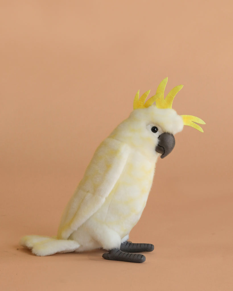 The Cockatoo Bird Stuffed Animal features soft yellow and white fur, a yellow crest, grey beak, and grey feet, set against a plain light peach background. Perfect for collectors of realistic plush animals.