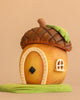 The Bumbu Handmade Wooden Acorn House features a whimsical acorn shape with a wooden door, small window, and leaf roof, sitting on a green patch against a beige background.