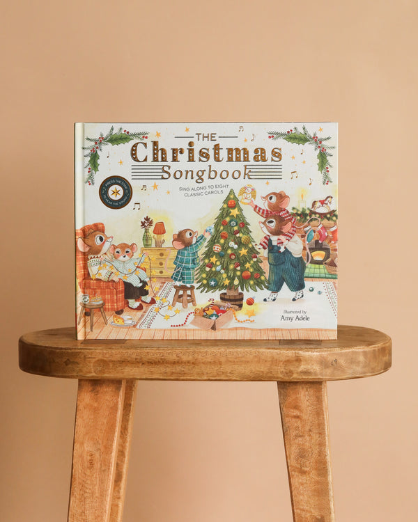 The Christmas Songbook," an interactive children’s picture book with a festive animal illustration on the cover, stands upright on a wooden stool against a beige background—perfect for sharing holiday carols together.
