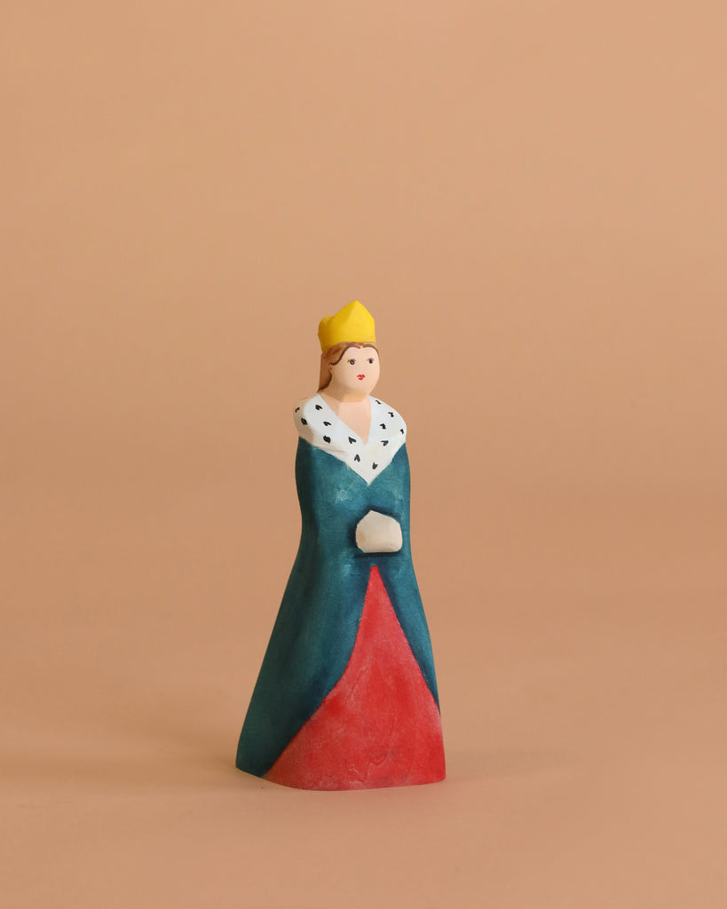 The Bumbu Handmade Wooden Queen is a handcrafted toy featuring a yellow crown, dark teal and red dress, and a white fur collar with black spots—ideal for imaginative fantasy role play against a beige background.