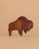 The Ostheimer Bison stands on a beige surface with a matching background. This handcrafted wooden figurine features a smooth finish and natural brown tones—ideal for lovers of natural wood toys.