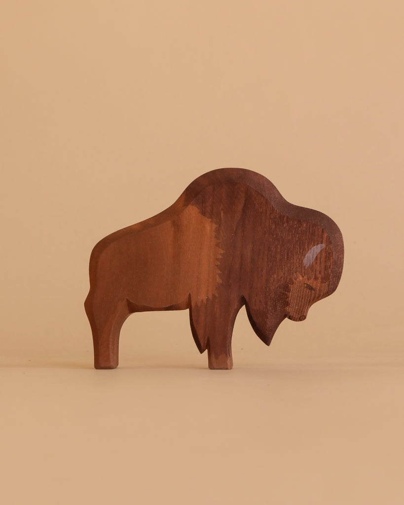 The Ostheimer Bison stands on a beige surface with a matching background. This handcrafted wooden figurine features a smooth finish and natural brown tones—ideal for lovers of natural wood toys.