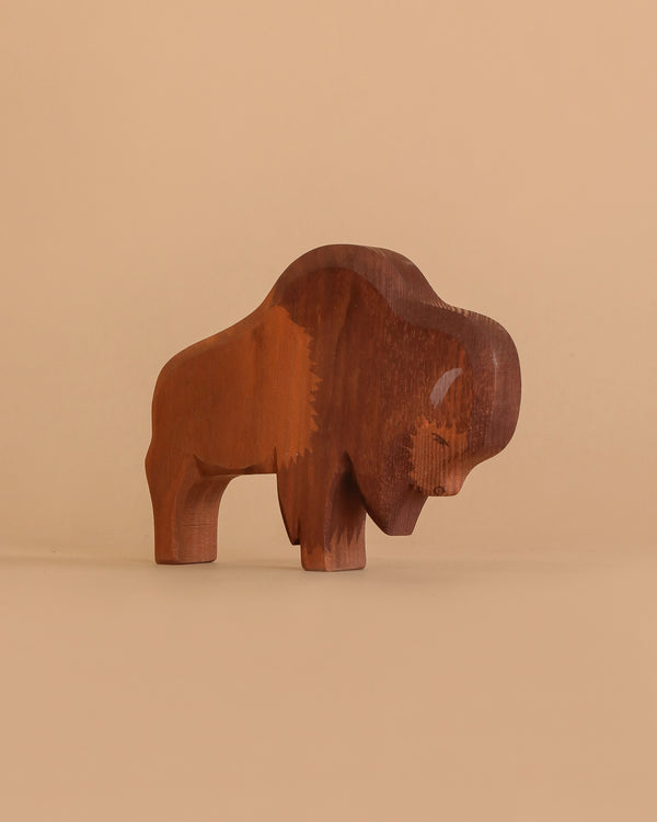 The Ostheimer Bison, a handcrafted wooden figurine inspired by classic Ostheimer wooden toys, stands on a light brown surface with a matching solid background.