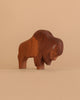 The Ostheimer Bison, a handcrafted wooden figurine inspired by classic Ostheimer wooden toys, stands on a light brown surface with a matching solid background.