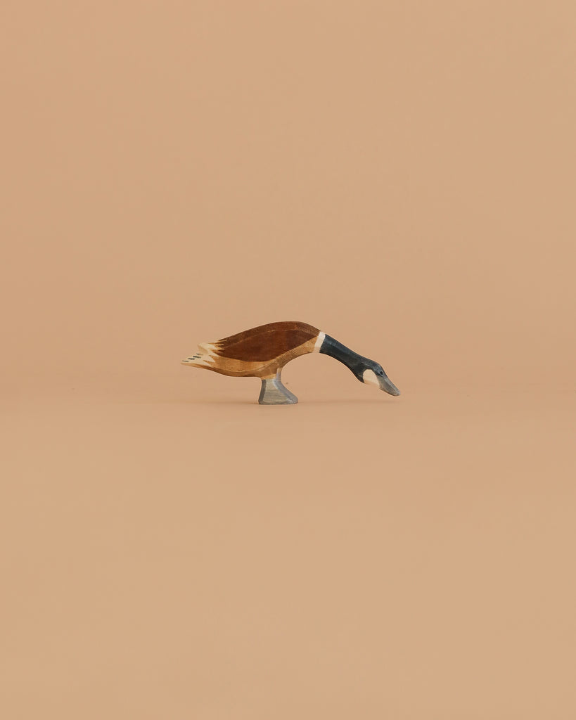 The Ostheimer Goose - Canada, Long Neck is a small handcrafted wooden figurine with its head bent down, made from sustainably sourced wood and inspired by classic Ostheimer toy design. Set against a plain light brown background.