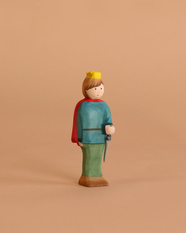 The Bumbu Handmade Wooden Prince features a wooden figure with a yellow crown, blue shirt, red cape, green pants, and brown shoes holding a gray sword—ideal for imaginative storytelling and Montessori toy collections. Beige background.