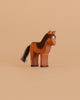 The Ostheimer Horse - Iceland Hrokur is a hand-carved wooden figurine with painted brown and black details and a black tail, standing upright against a plain beige background.