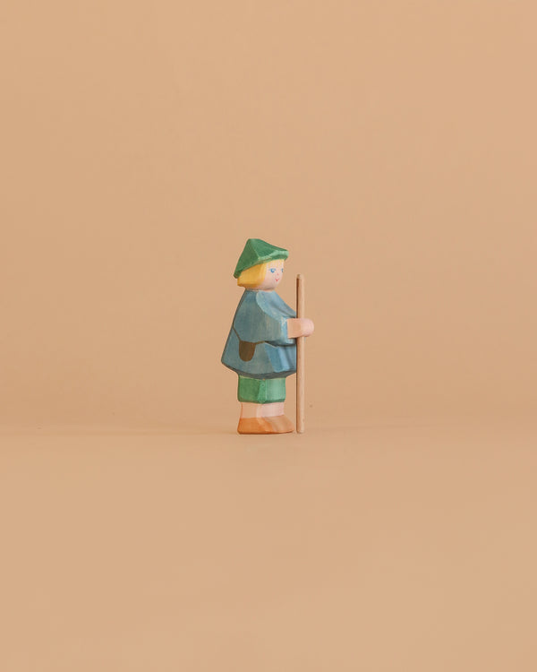 The Ostheimer Shepherd Boy is a small handcrafted wooden figurine featuring green and blue clothing and a green hat, holding a stick—ideal for imaginative play or as a charming addition to your Ostheimer toys collection.