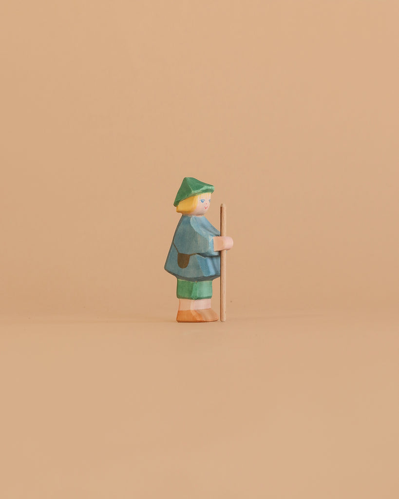 The Ostheimer Shepherd Boy is a small handcrafted wooden figurine featuring green and blue clothing and a green hat, holding a stick—ideal for imaginative play or as a charming addition to your Ostheimer toys collection.