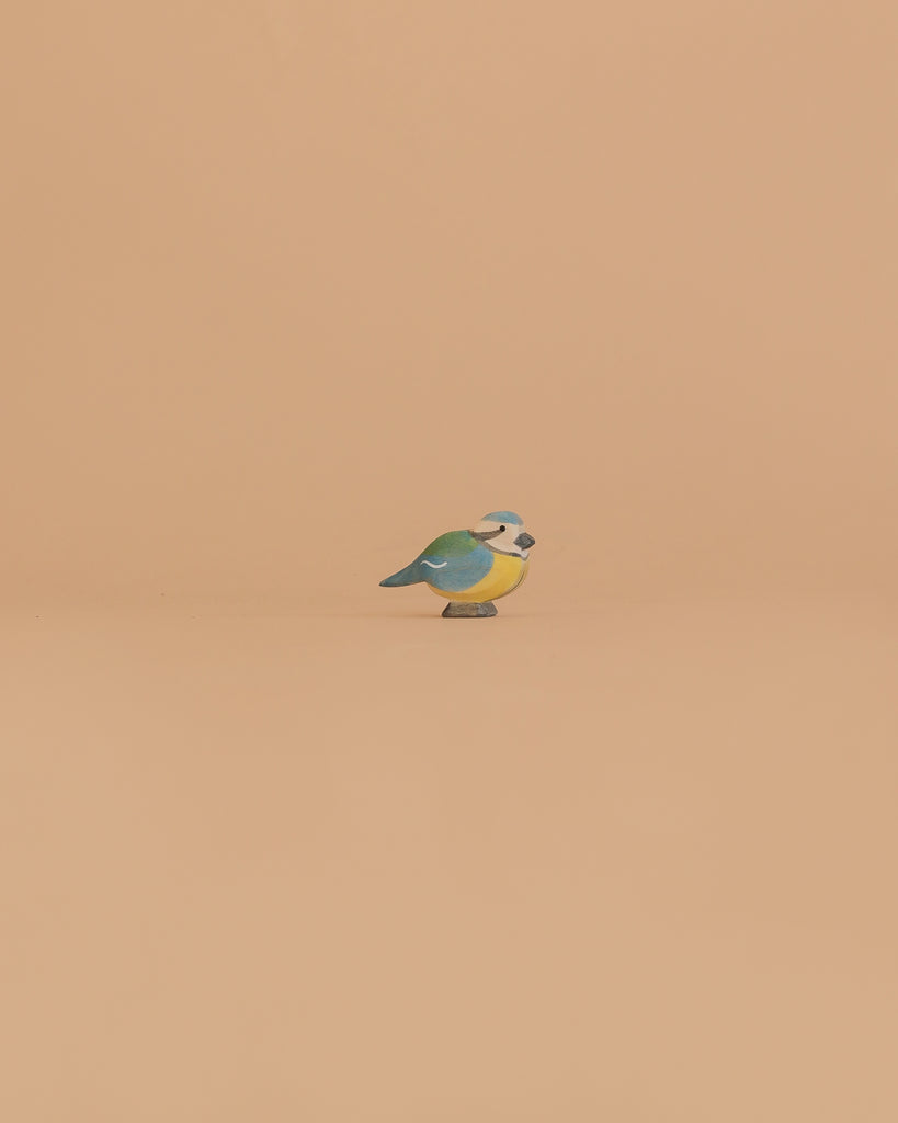 The Ostheimer Bird - Blue Tit is a small wooden figurine with vibrant green, blue, and yellow markings, perfect for imaginative play or as a charming addition to your handcrafted Ostheimer toys collection.
