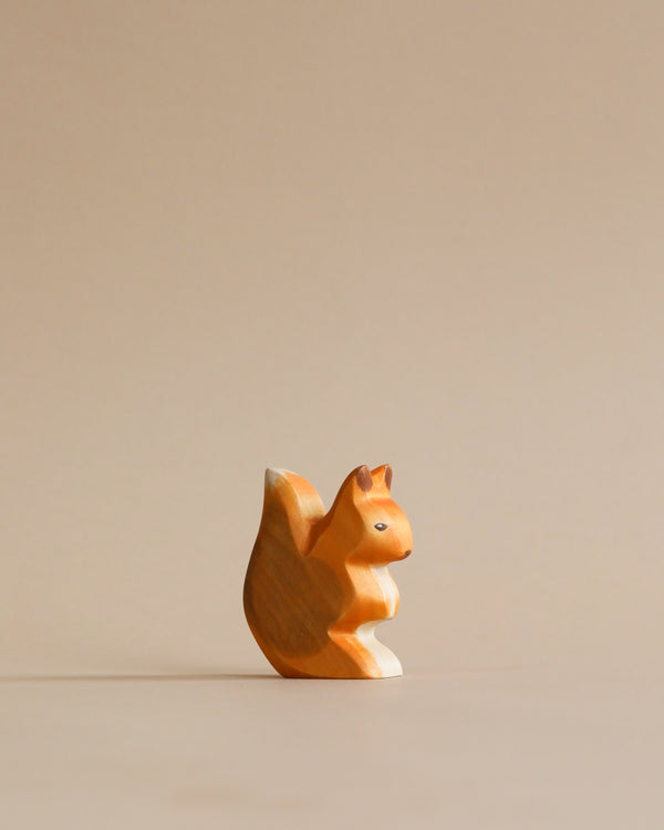 A Handmade Holzwald Squirrel stands against a plain, light beige background, featuring intricate grain details and a smooth finish.