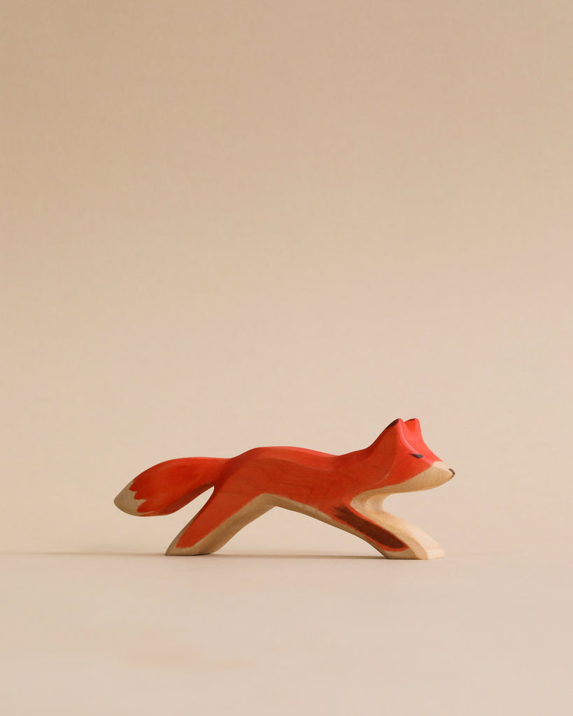 A Handmade Holzwald Running Fox figurine, painted with natural dyes and white details, positioned centrally against a plain light beige background.