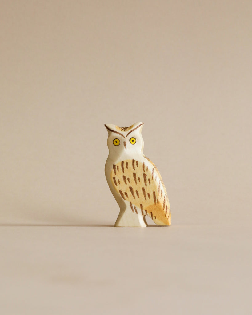 A small Handmade Holzwald Owl figurine, expertly carved with detailed feathers and bright yellow eyes, standing against a plain, light beige background. This piece is part of our collection of high-quality wooden toys.