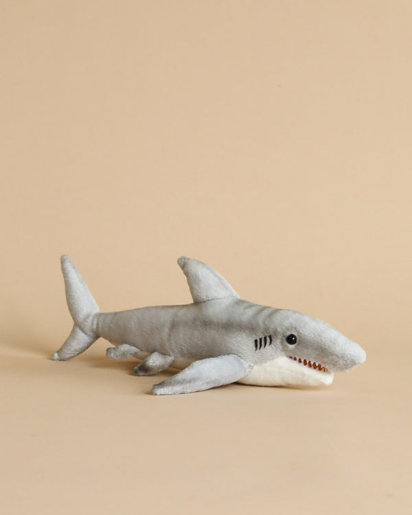 A plush toy Tiger Shark Stuffed Animal with a light gray color and white underbelly, featuring detailed stitching and a slightly open mouth, resembling HANSA's realistic stuffed animals, set against a plain beige background.
