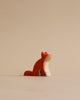 A sustainable Handmade Holzwald Sitting Fox figurine sits elegantly against a plain light beige background, its head tilted upwards as if gazing at something in the distance.