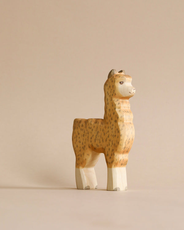 A Handmade Holzwald Alpaca, crafted with natural dyes, exhibits a cheerful expression while standing upright against a plain, light beige background.